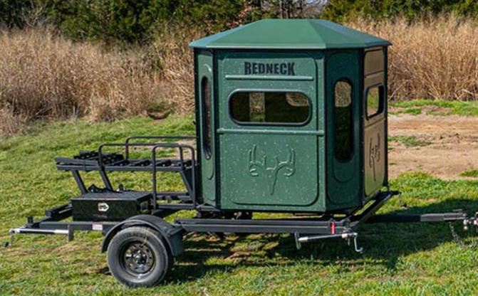 8 foot hydraulic blind trailer lowered in a field with a green Buck Palace blind mounted on top.