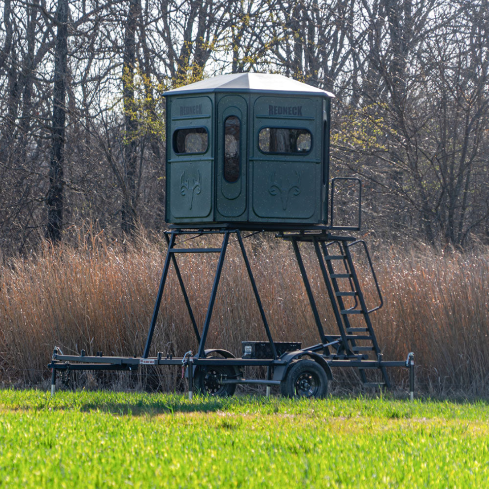 8 foot hydraulic blind trailer raised in a field with a box blind mounted on top.